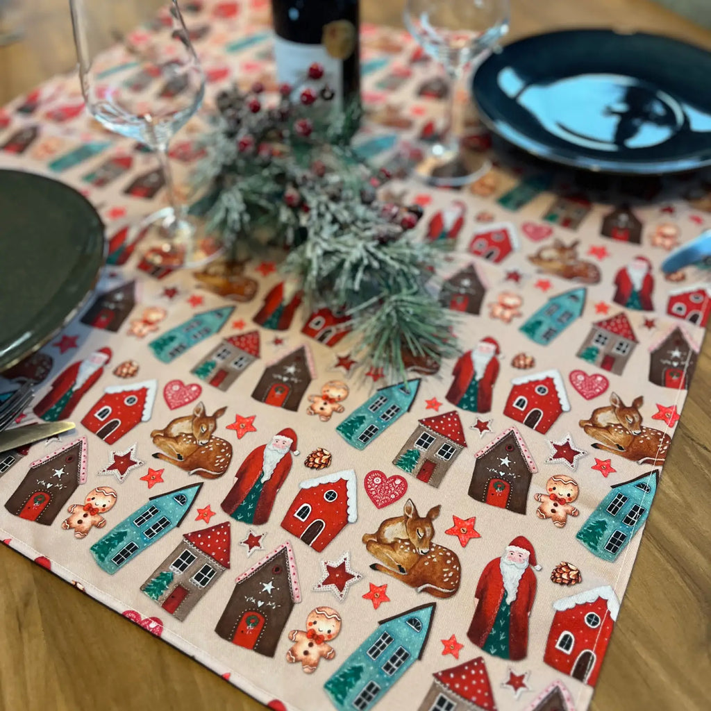 Petite nappe carrée de Noël avec motif maisons et personnages, mise en scène sur une table – création Rose & Myrtille